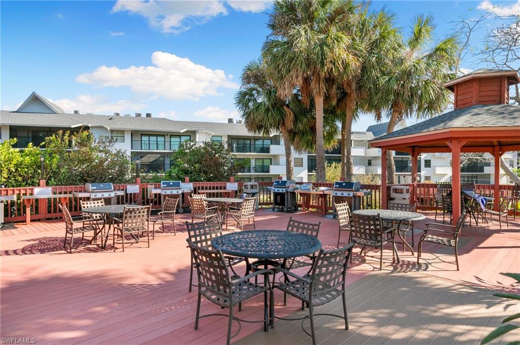 600 Neapolitan Way, Unit 257 Naples, FL 34103 - Photo 26 of 35 a view of a patio with dining table and chairs under an umbrella with palm trees