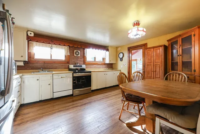 a kitchen with granite countertop a stove a sink dishwasher a dining table and chairs with wooden floor