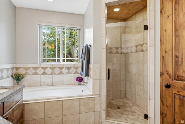 3148 Lower Saddleback Road Park City, UT 84098 - Photo 41 of 67 Bathroom featuring a built-in soaking tub with surrounding tile, a glass-enclosed shower with tile walls and a patterned accent band, a window with exterior tree scenery, wood-finish cabinetry, and a dark wood door
