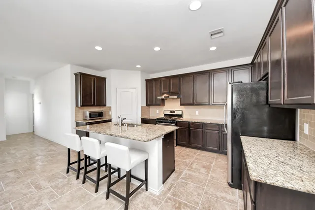a kitchen with stainless steel appliances kitchen island granite countertop a sink refrigerator and cabinets