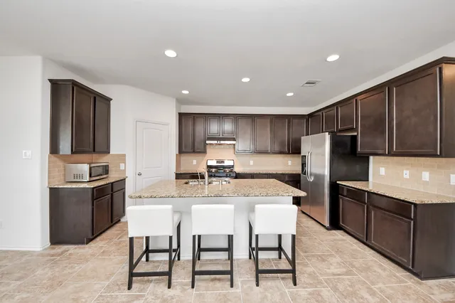 a kitchen with stainless steel appliances kitchen island granite countertop a refrigerator a stove a sink a oven with a dining table and chairs