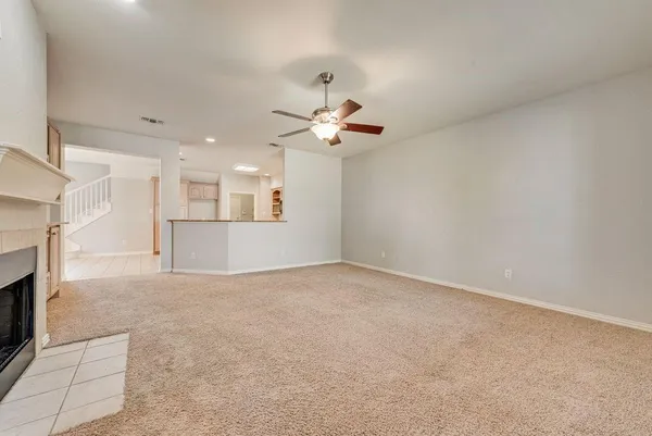 an empty room with a ceiling fan and a kitchen view