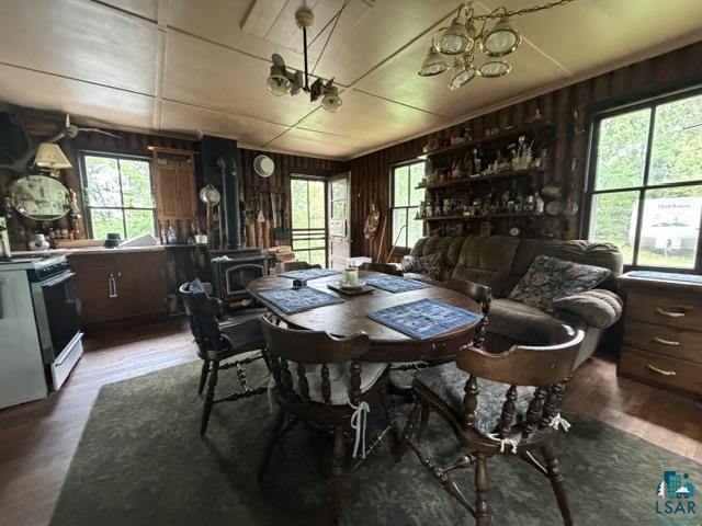 9064 Peppard Road Britt, MN 55710 - Photo 5 of 40 Open concept room featuring wood-finish flooring, a wood-burning stove, exposed wood paneling on walls, white paneled ceiling, and multiple windows