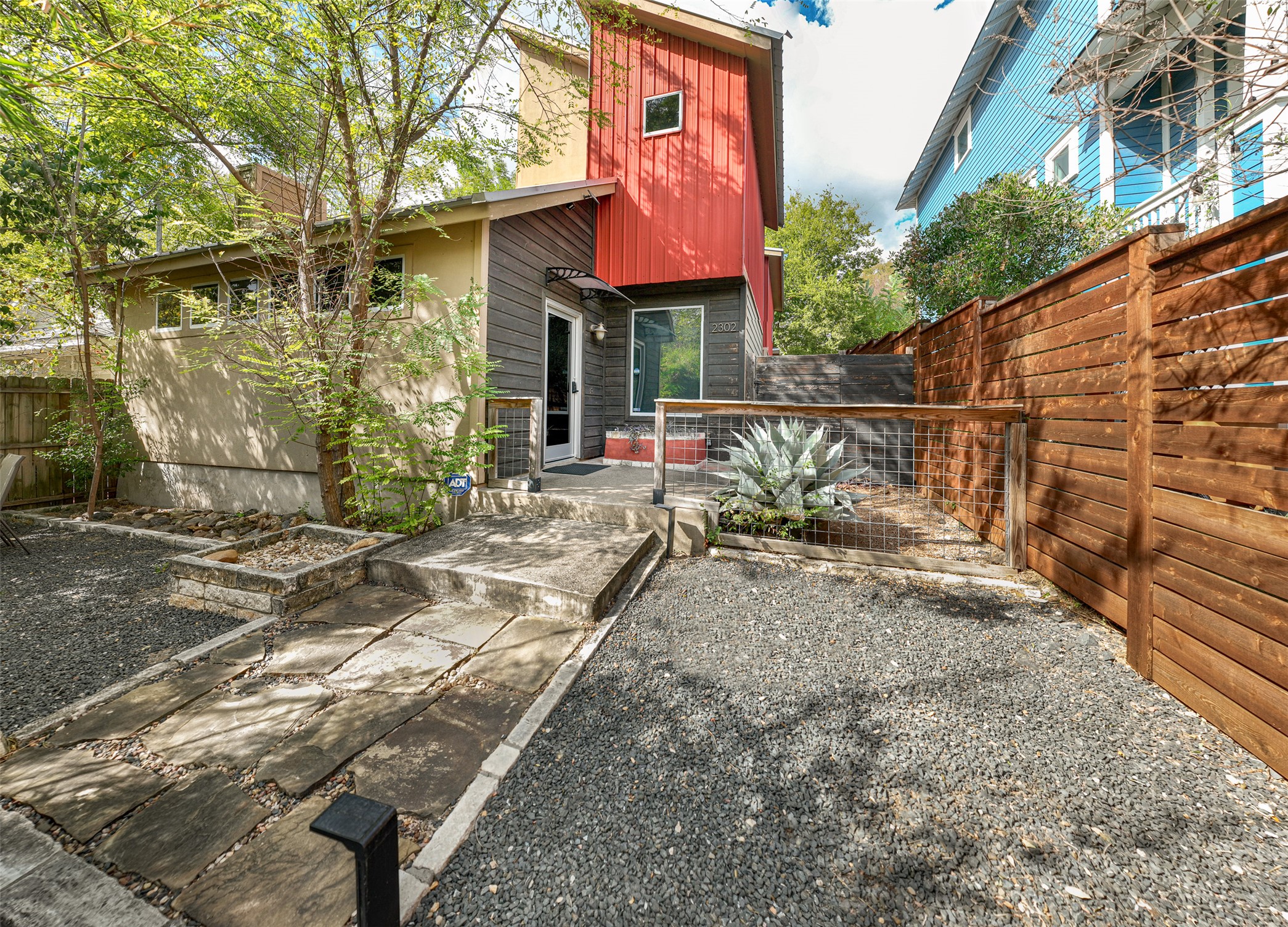 2302 East 9th Street Austin, TX 78702 - Photo 3 of 31 A unique, modern exterior with vibrant red and gray siding, accented by natural wood fencing.