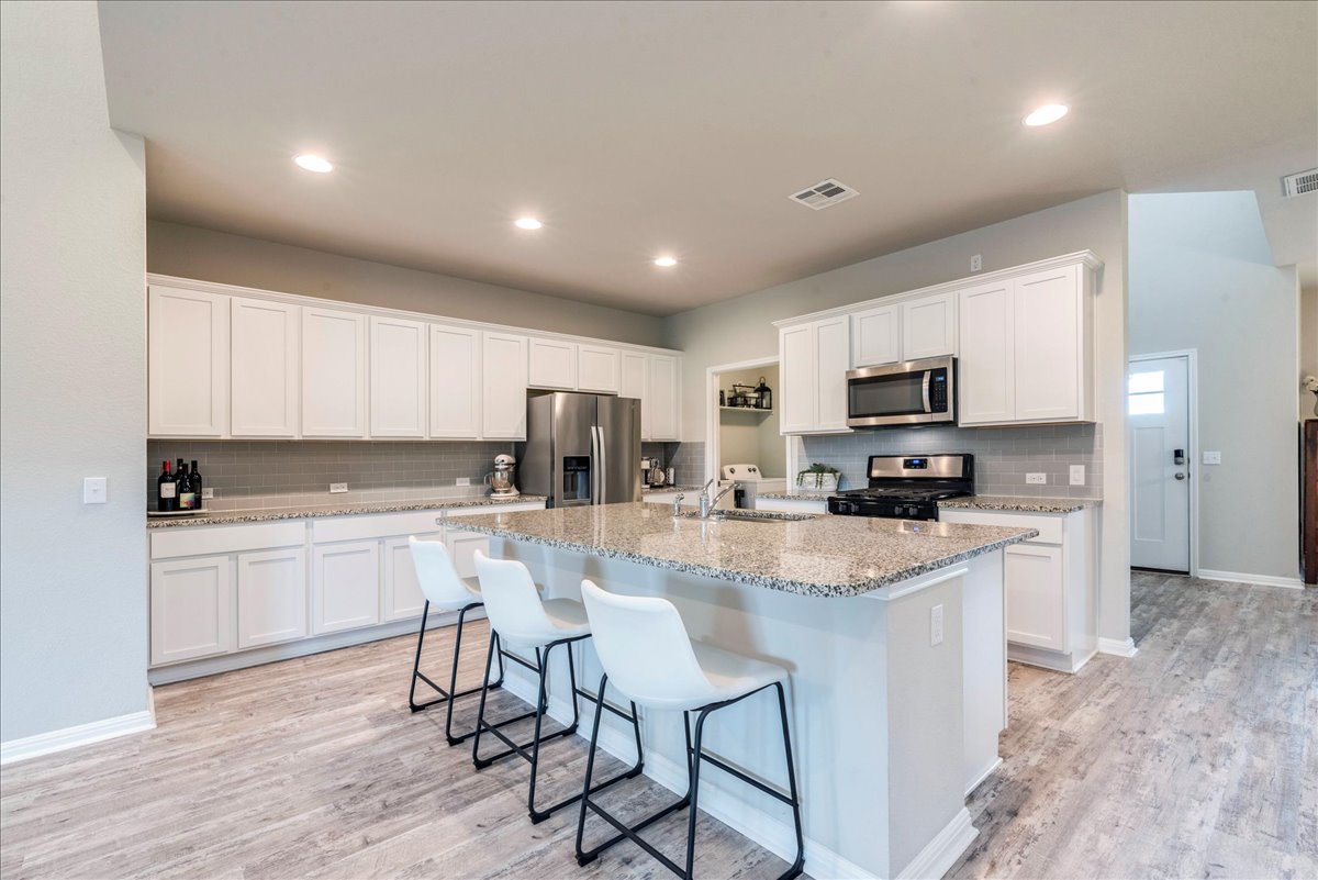 125 Groesbeck Lane Leander, TX 78641 - Photo 8 of 38 a kitchen with stainless steel appliances granite countertop a stove top oven a sink dishwasher a refrigerator and white cabinets with wooden floor