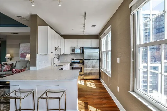 a kitchen with stainless steel appliances granite countertop a refrigerator a sink a stove and white cabinets with wooden floor