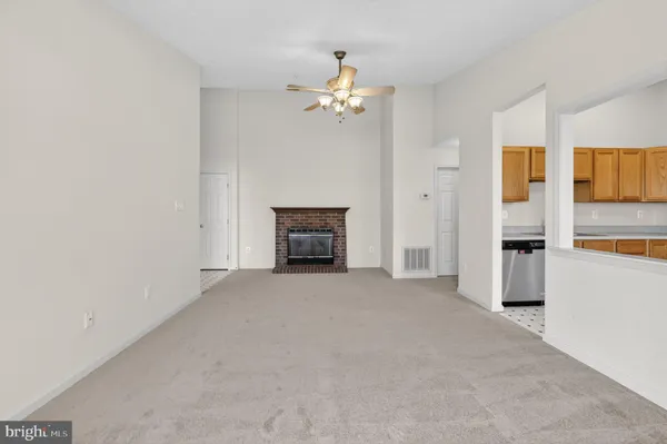 an empty room with chandelier fan and kitchen view