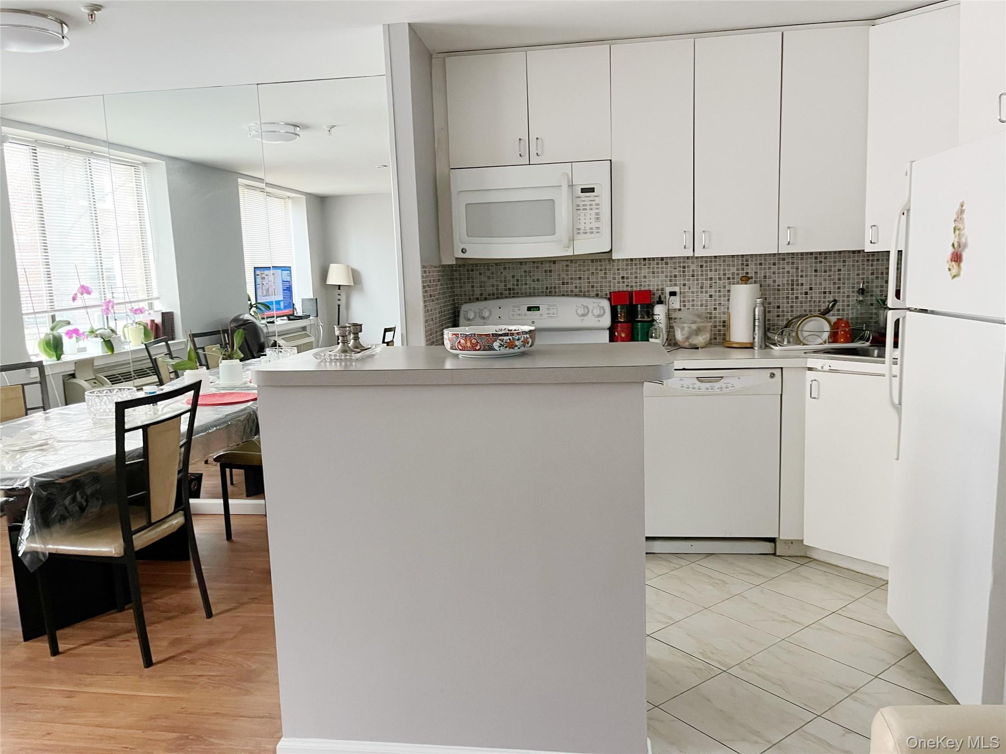 10 Canterbury Road, Unit 1B Great Neck, NY 11021 - Photo 9 of 10 a kitchen with stainless steel appliances granite countertop a stove top oven a sink a dining table and chairs with white cabinets