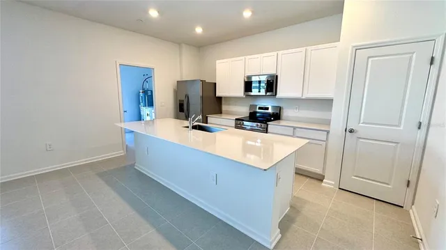 a room with kitchen island a sink a refrigerator and cabinets