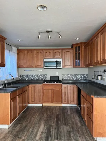 a kitchen with stainless steel appliances granite countertop wooden cabinets a stove top oven a sink and dishwasher with wooden floor