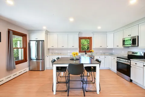 a kitchen with stainless steel appliances granite countertop a stove a sink a refrigerator a stove a dining table and chairs with wooden floor