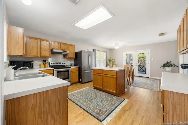 a kitchen with a refrigerator a stove top oven a sink dishwasher and wooden cabinets with wooden floor