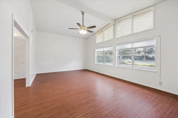 an empty room with wooden floor chandelier fan and windows