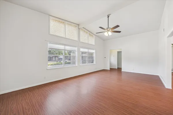 an empty room with wooden floor chandelier fan and windows