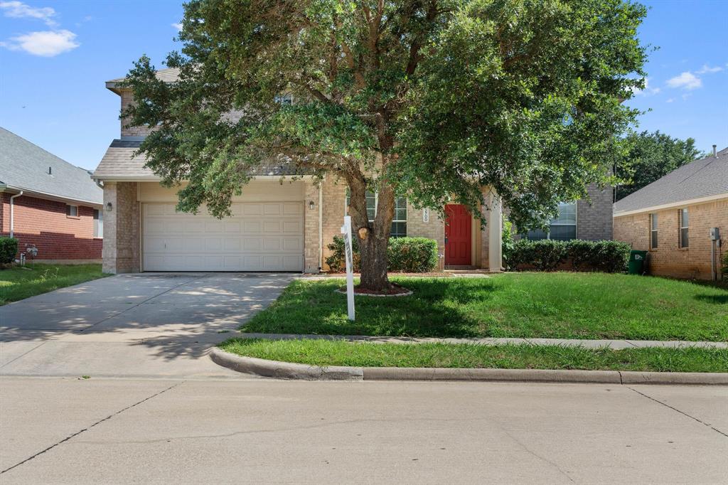 2700 Hereford Road Denton, TX 76210 - Photo 1 of 36 Two-story brick and stone veneer exterior featuring a two-car garage, a concrete driveway, a prominent mature tree, a red front door, and a manicured lawn