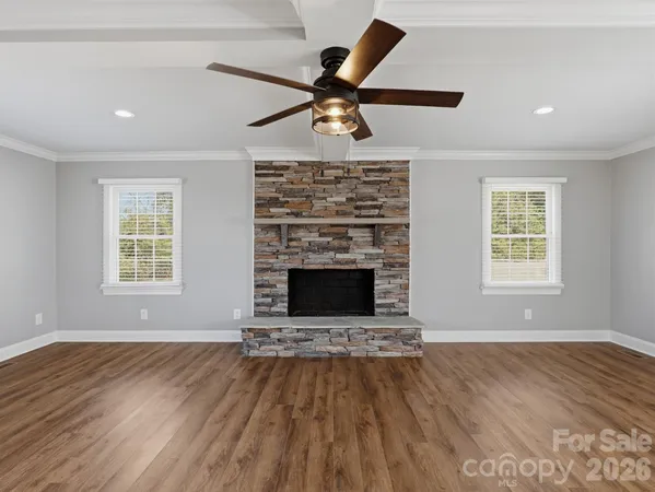 an empty room with windows a fireplace a ceiling fan and wooden floor