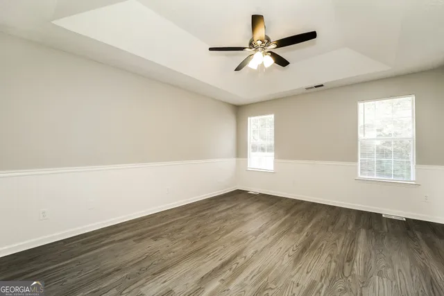 an empty room with wooden floor fan and windows