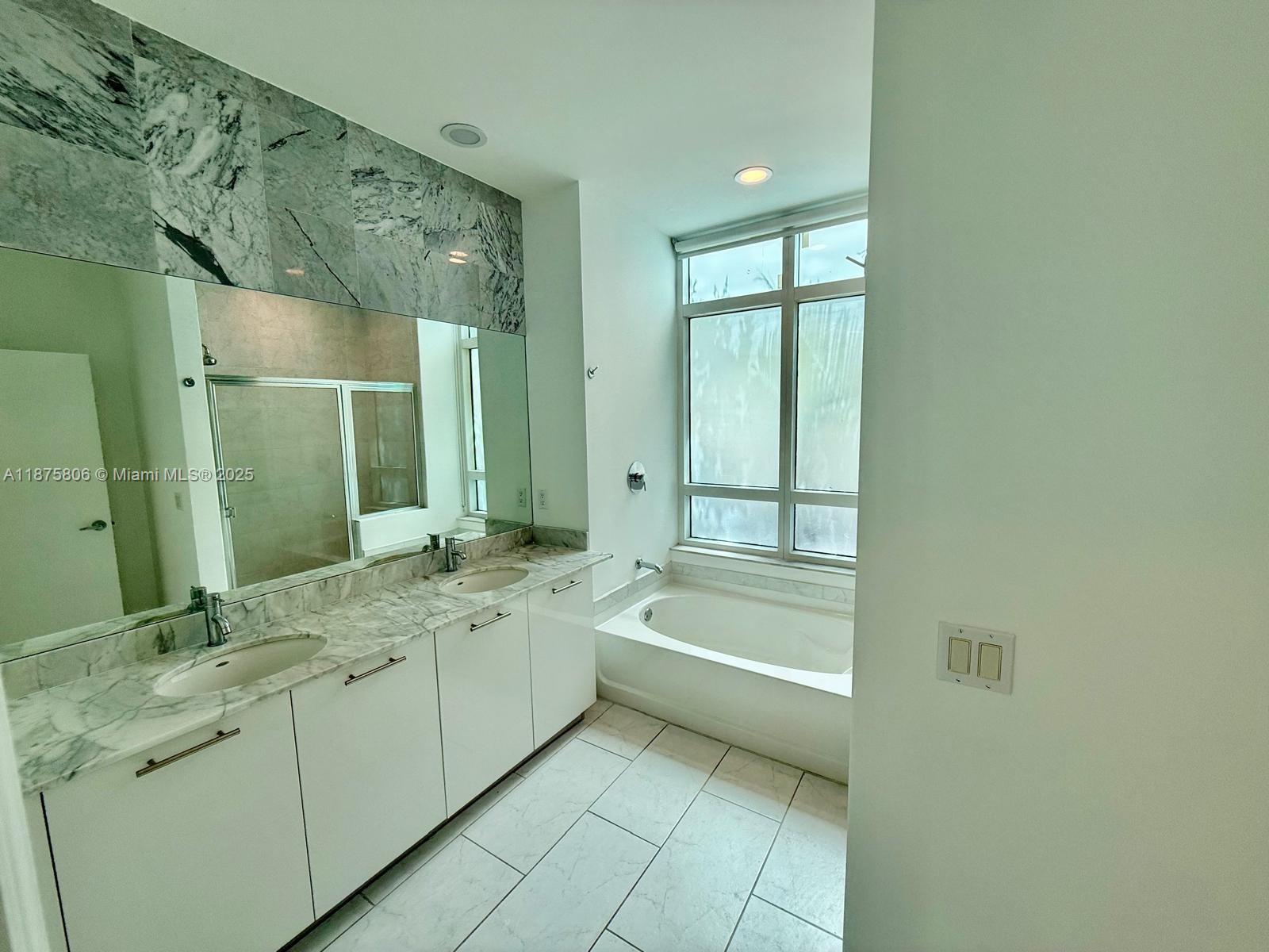 951 Brickell Avenue, Unit 1010 Miami, FL 33131 - Photo 11 of 23 a bathroom with a granite countertop sink a large mirror a bathtub and next to a window