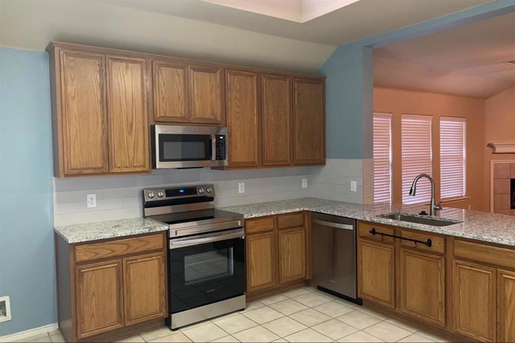 3321 Truman Street McKinney, TX 75071 - Photo 10 of 26 a kitchen with granite countertop a sink a stove a microwave and wooden cabinets