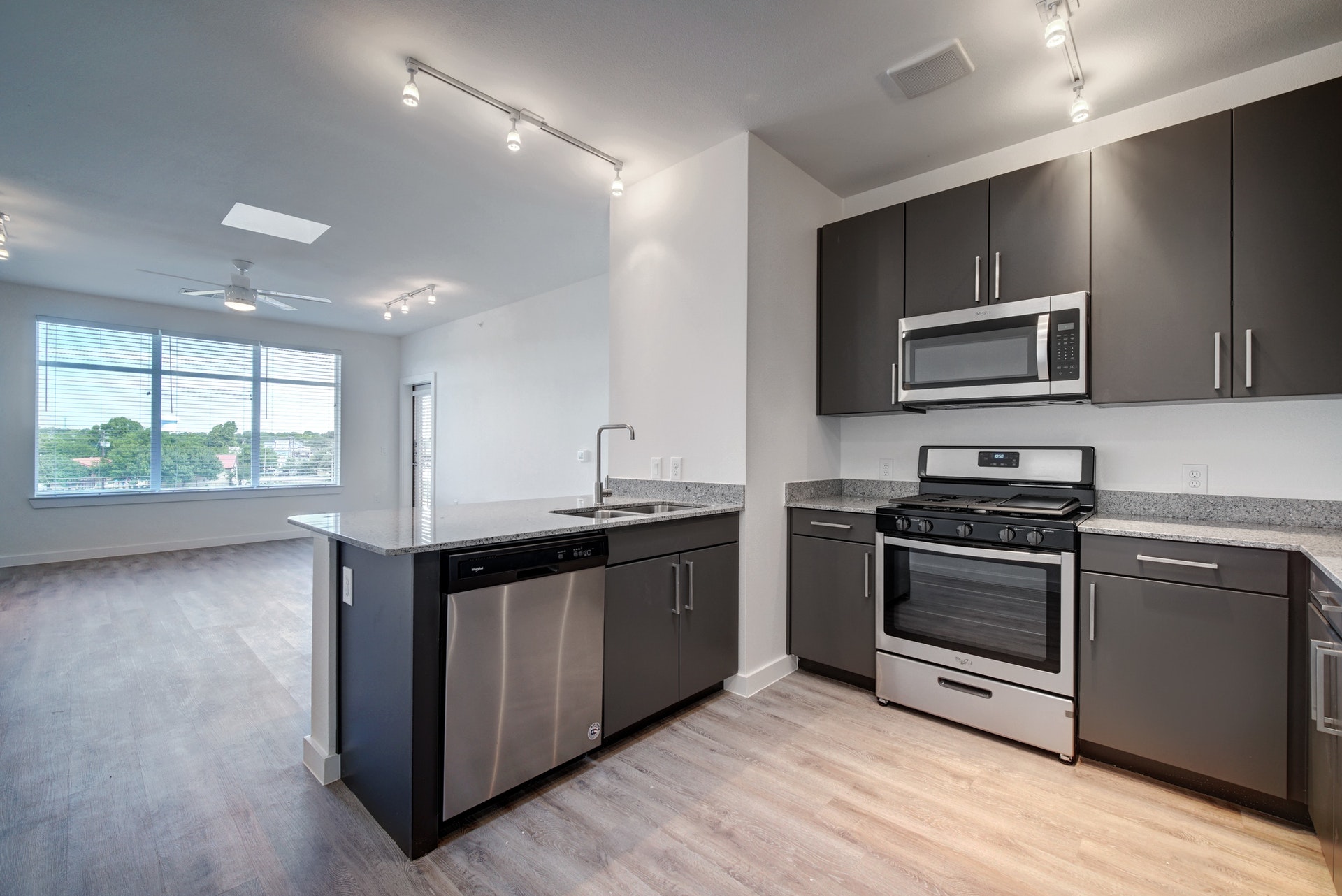 13130 Pond Springs Road, Unit 3214 Austin, TX 78729 - Photo 12 of 40 Kitchen with rail lighting, appliances with stainless steel finishes, a peninsula, light stone counters, and light wood-style flooring