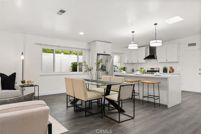 a dining room with kitchen island stainless steel appliances furniture large window and wooden floor