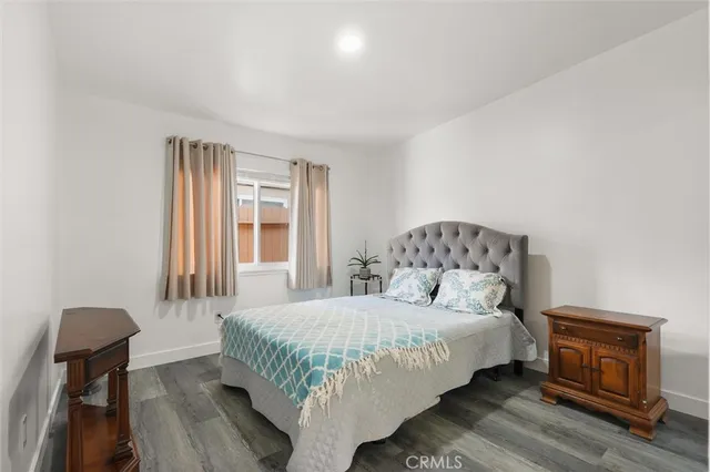 a bedroom with a bed and dresser with wooden floor