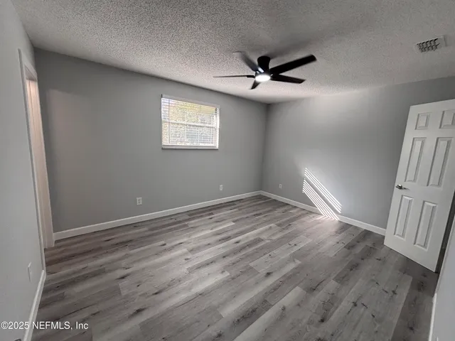 an empty room with wooden floor fan and windows