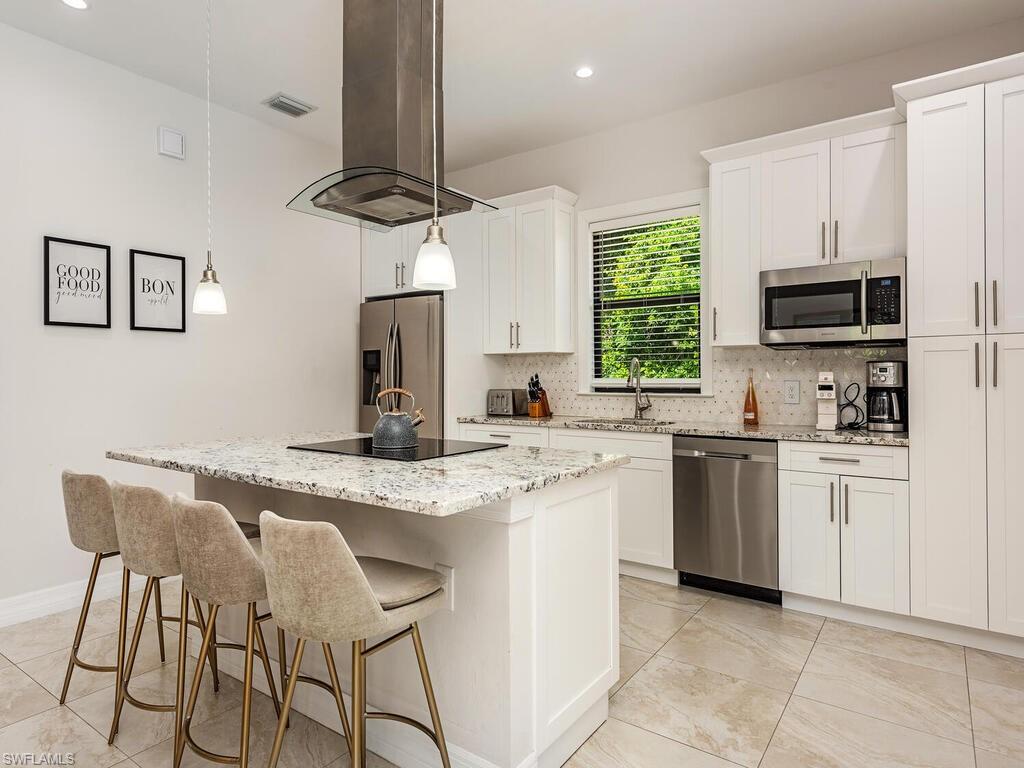 1021 Creech Road Naples, FL 34103 - Photo 4 of 12 Kitchen with decorative backsplash, island exhaust hood, a center island, light stone countertops, and appliances with stainless steel finishes