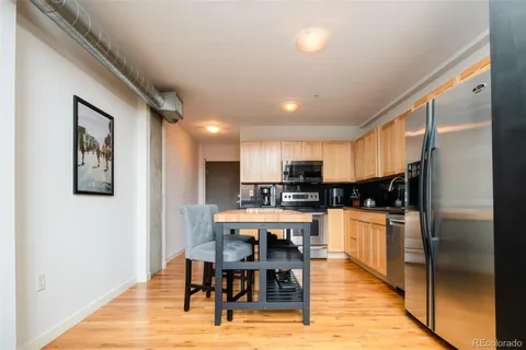 a kitchen with stainless steel appliances kitchen island granite countertop a refrigerator a stove a sink a dining table and chairs with wooden floor