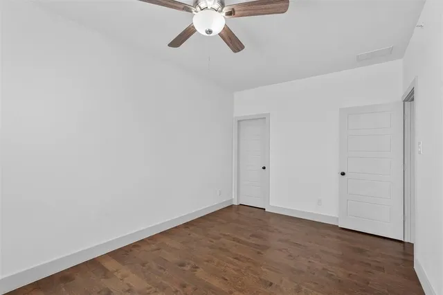 a view of an empty room with wooden floor and a ceiling fan
