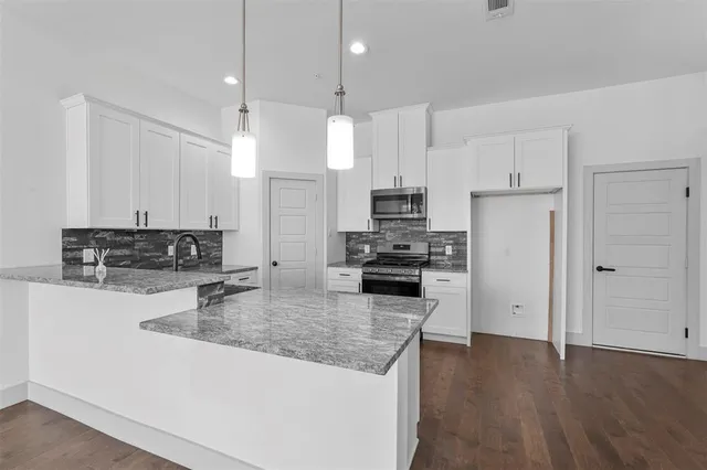 a kitchen with stainless steel appliances granite countertop a refrigerator a sink a stove and white cabinets with wooden floor