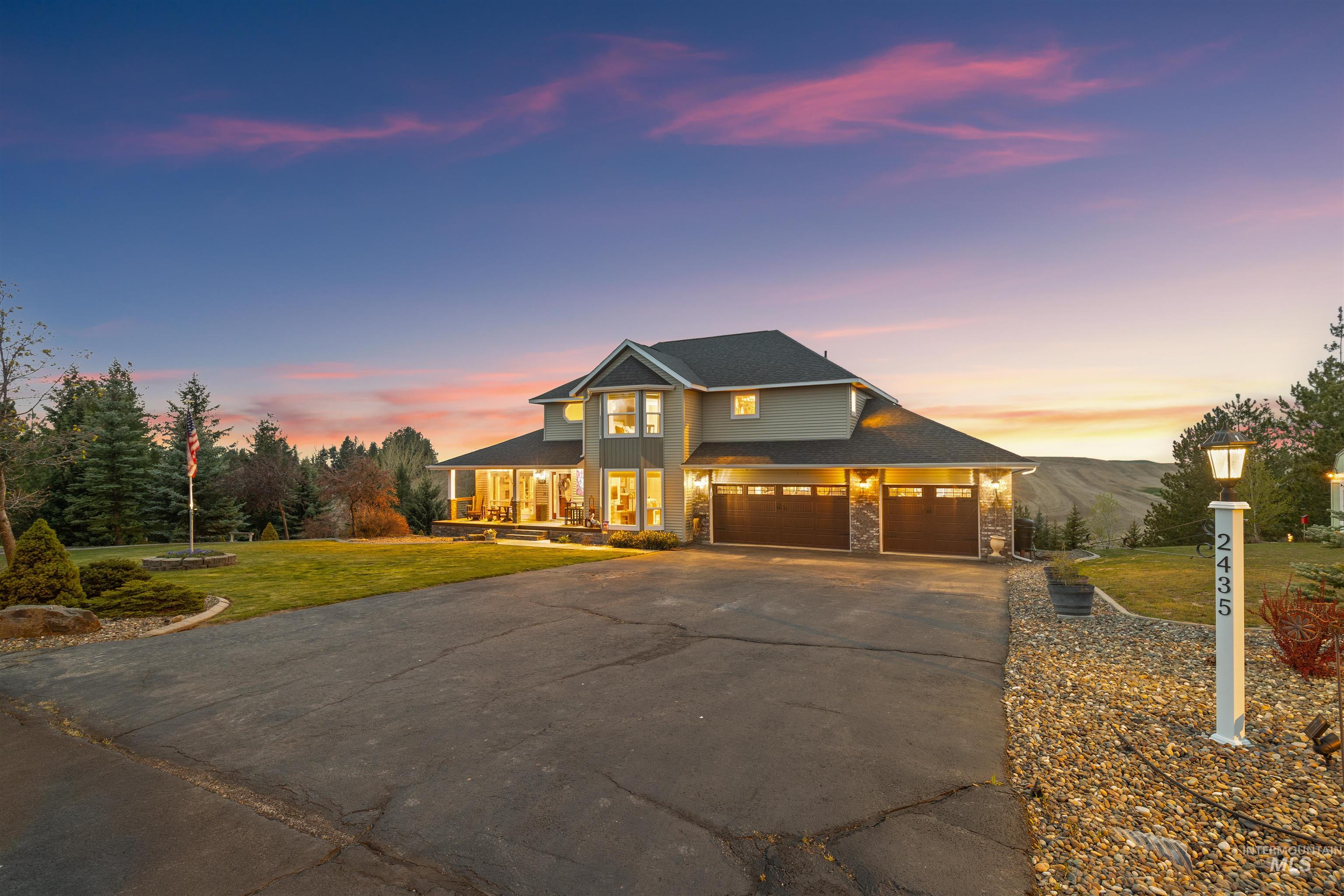 View of front of property featuring driveway, a front lawn, stone siding, a garage, and roof with shingles