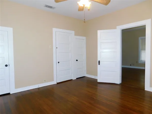 an empty room with wooden floor chandelier fan and windows