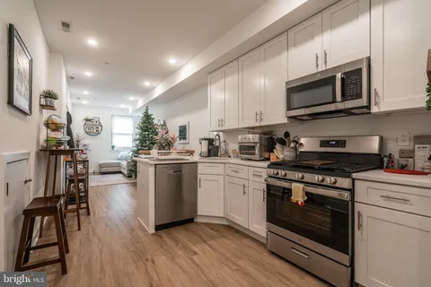 a kitchen with stainless steel appliances granite countertop a stove top oven a sink dishwasher a refrigerator white cabinets and wooden floor