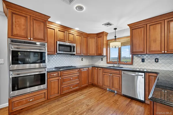 a kitchen with stainless steel appliances granite countertop wooden cabinets a stove a sink and dishwasher with wooden floor