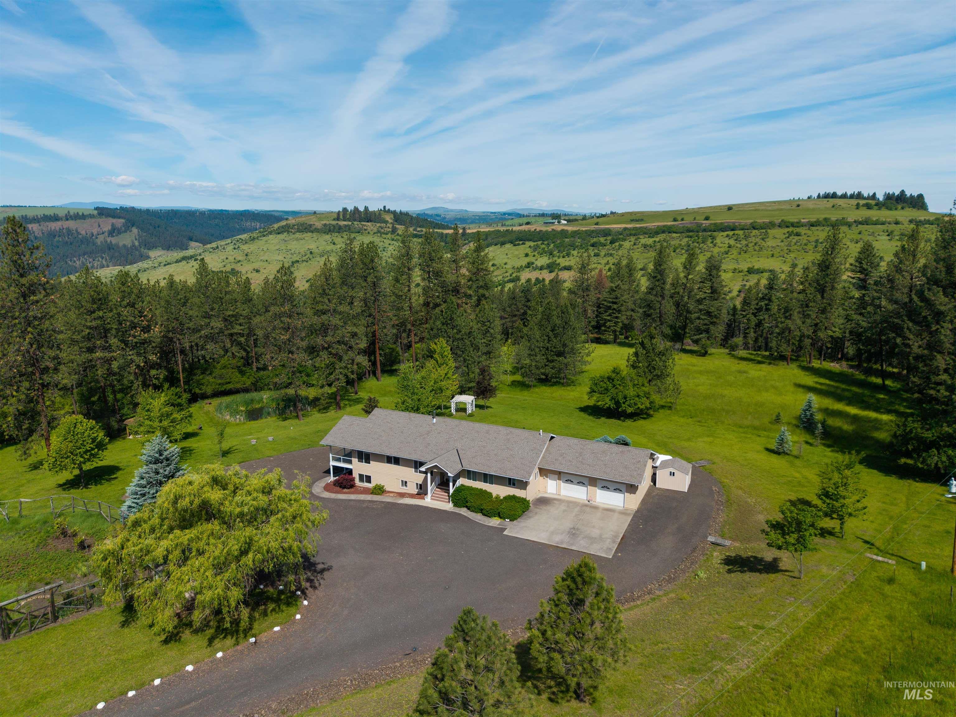 Expansive rural property featuring a two-story residence with a three-car garage, established landscaping, and a private pond