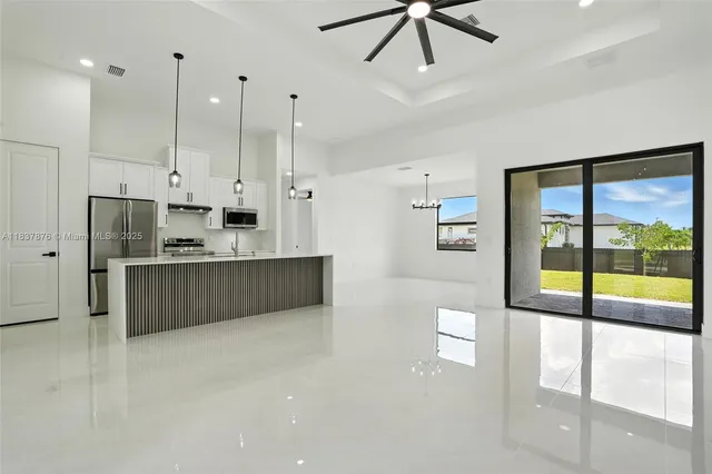 a large kitchen with stainless steel appliances a large counter top a refrigerator a oven a large island with the ceiling fan