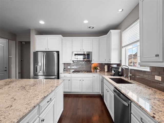 a kitchen with kitchen island granite countertop a sink stove refrigerator and white cabinets with wooden floor