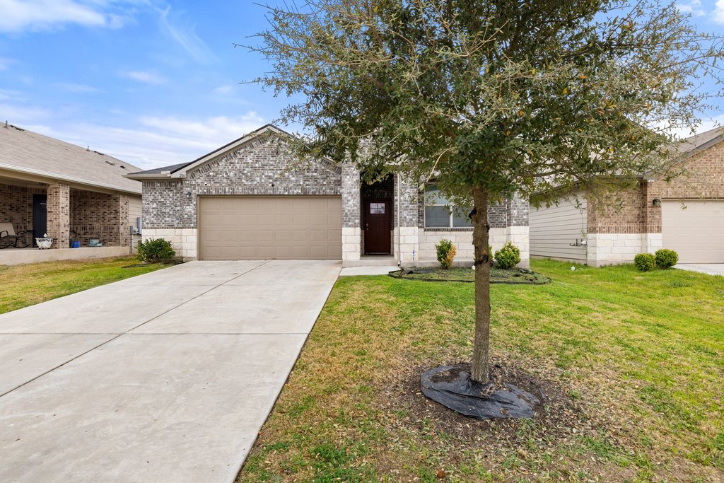 Obstructed view of property with brick siding, an attached garage, a front lawn, and concrete driveway