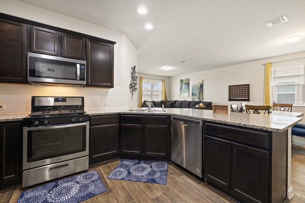204 Rochester Lane Hutto, TX 78634 - Photo 39 of 40 Kitchen with stainless steel appliances, a peninsula, open floor plan, light stone countertops, and dark wood finish cabinetry