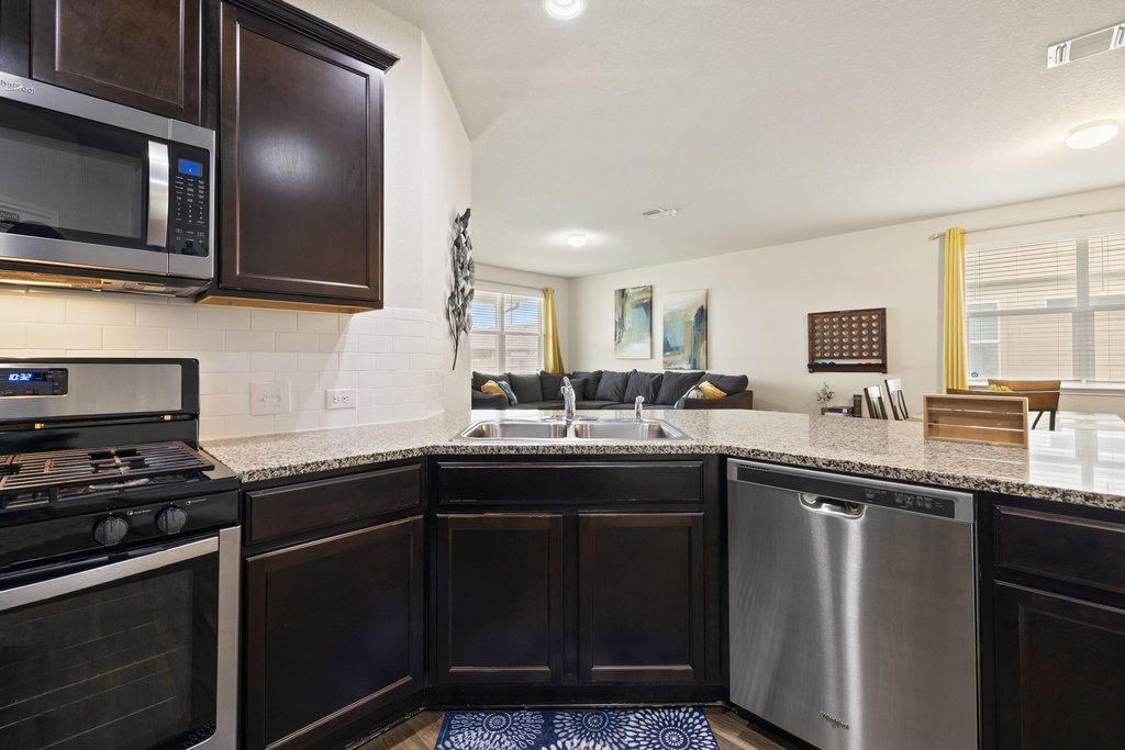 204 Rochester Lane Hutto, TX 78634 - Photo 40 of 40 Kitchen with stainless steel appliances, dark wood finish cabinets, open floor plan, backsplash, and light stone counters