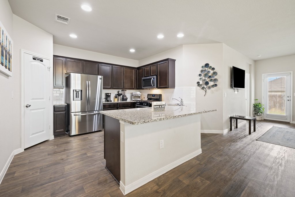 204 Rochester Lane Hutto, TX 78634 - Photo 8 of 40 Kitchen featuring dark wood finish cabinets, stainless steel appliances, light stone countertops, dark wood-type flooring, and recessed lighting