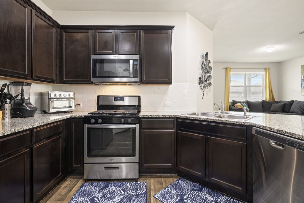 204 Rochester Lane Hutto, TX 78634 - Photo 38 of 40 Kitchen featuring stainless steel appliances, dark wood finish cabinetry, open floor plan, light wood-style floors, and tasteful backsplash