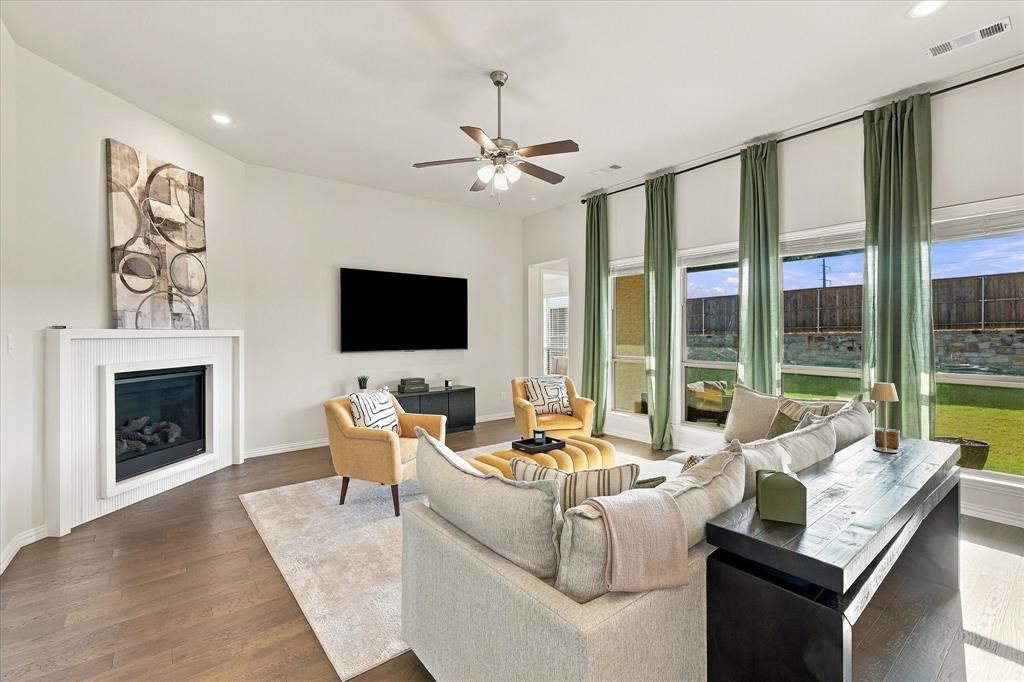 137 Chisos Court Rhome, TX 76078 - Photo 6 of 40 Spacious living area featuring wood-finish flooring, a white fireplace, a ceiling fan, and large windows with roller shades