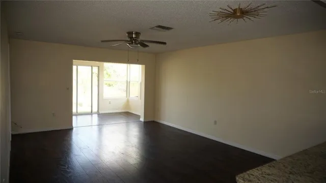 an empty room with wooden floor fan and windows