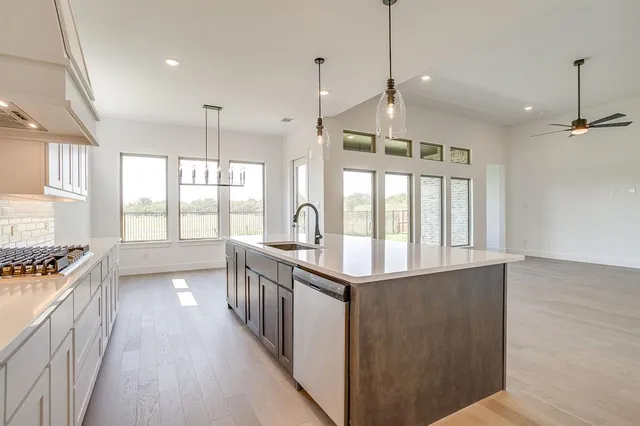 a kitchen with stainless steel appliances granite countertop a stove a sink a refrigerator and white cabinets with wooden floor