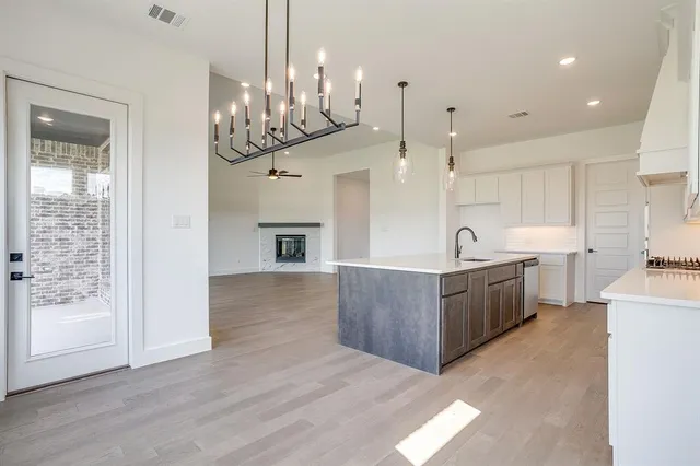 a large kitchen with stainless steel appliances granite countertop a large kitchen island a refrigerator a stove a sink and a dining table with wooden floor