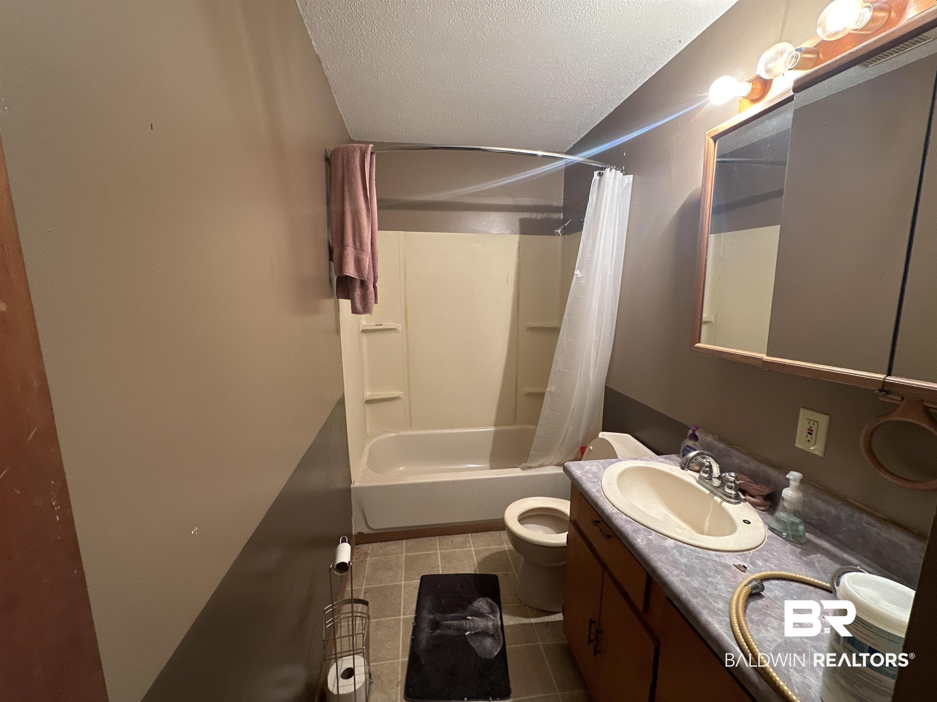 9520 C Four Mile Road Irvington, AL 36544 - Photo 19 of 32 Full bathroom featuring vanity, tile patterned flooring, toilet, a textured ceiling, and shower / tub combo with curtain