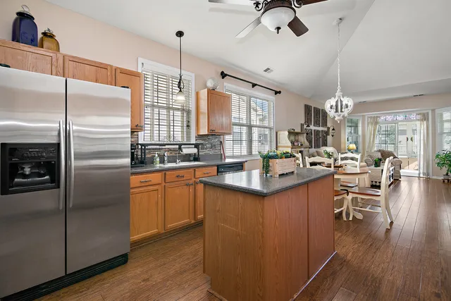 a kitchen with stainless steel appliances granite countertop a refrigerator a sink dishwasher a stove and a dining table with wooden floor