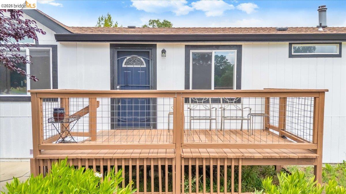 4419 Little John Road Copperopolis, CA 95228 - Photo 38 of 43 Exterior featuring a wood deck with wire grid railing, a blue entry door with an arched window, and white siding with dark trim